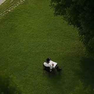 A solitary figure sits in a chair on a vast green lawn, reading beneath a tree—visually capturing the post's message of staying offline while the Crypto.com App monitors price movements on their behalf.