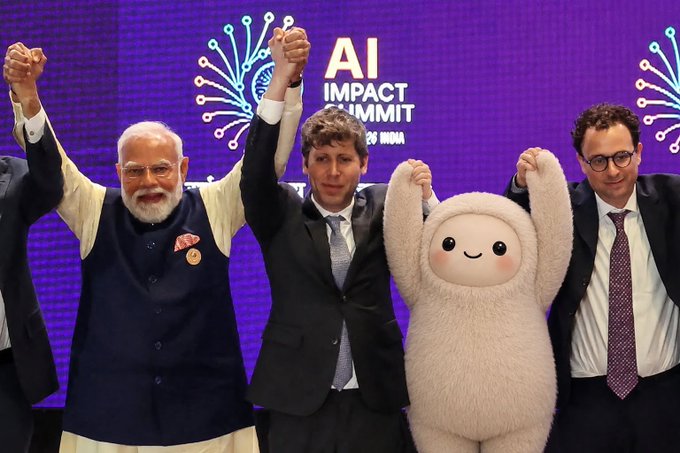 The caption for the post would be something like this:

> Indian Prime Minister Narendra Modi, OpenAI CEO Sam Altman, and Anthropic CEO Dario Amodei pose with raised hands alongside a plush sloth mascot at the AI Impact Summit in India.

**Relation to the post:** The whimsical mention of "Muse" (a fictional AI concept from the *Ultraviolet* film) seems to be poking fun at the presence of the cute, fluffy sloth mascot standing among major AI industry leaders — suggesting even a sleepy sloth could join the summit lineup. The image perfectly captures this absurd juxtaposition: serious AI executives and a world leader celebrating alongside a cartoonish plush character.