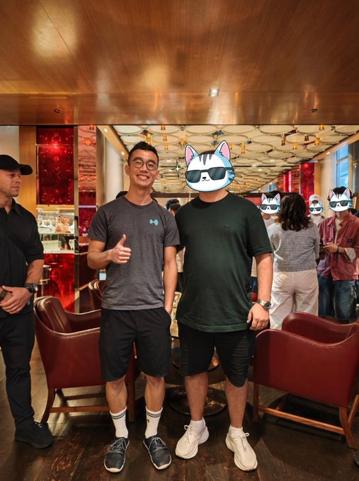 Two men pose for a photo in an upscale lounge, with one giving a thumbs-up, both wearing casual attire, capturing an in-person meeting from the Hyperliquid community as referenced in the post. The scene reflects the post's sentiment of finally connecting faces with online trading peers, celebrating the moment of meeting teammates like Jeff from the HL team.