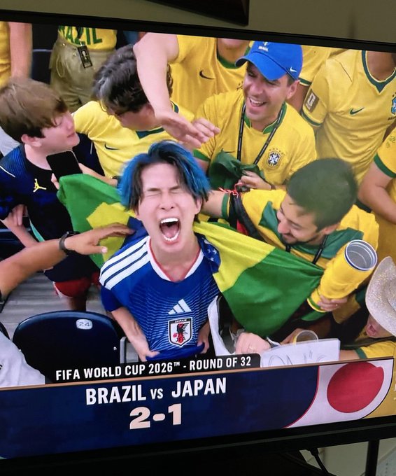 A screenshot of a TV displaying the "FIFA WORLD CUP 2026™ - ROUND OF 32: BRAZIL vs JAPAN 2-1" match shows a blue-haired fan in a Japan jersey crying in anguish while surrounded by ecstatic Brazilian fans celebrating their victory, humorously illustrating the disappointment of crypto users who missed out on the $ansem airdrop.