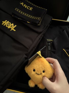 A hand holding a small plush toy in front of an open OKX-branded box containing merchandise and a black envelope labeled "MOMENTANCE."