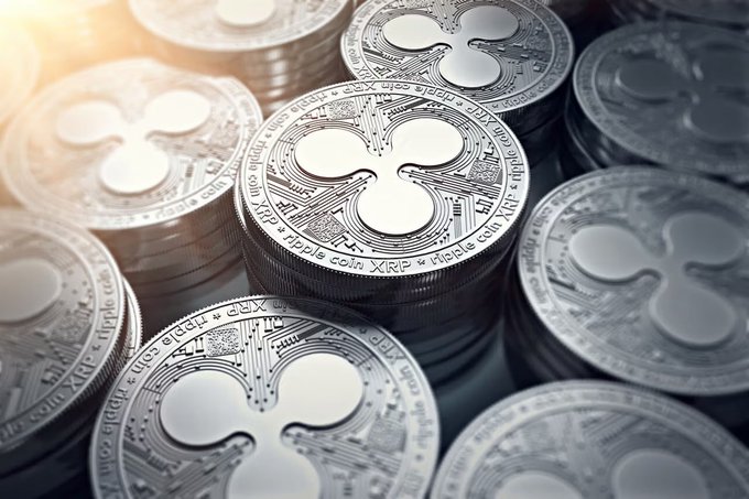 A close-up view shows several stacks of silver Ripple (XRP) cryptocurrency coins catching the light.