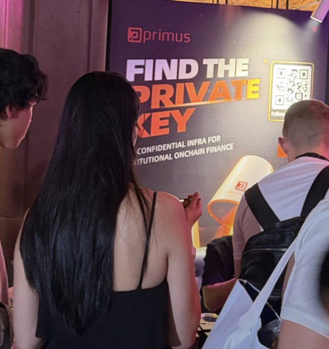 People gather near a 'primus' advertisement reading 'FIND THE PRIVATE KEY' and 'CONFIDENTIAL INFRA FOR INSTITUTIONAL ONCHAIN FINANCE' at an event.