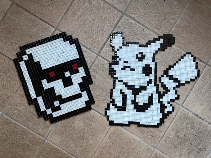 Two completed pixel art bead sprites featuring a skull with red eyes and a Pikachu sit on a tiled floor, ready to be displayed as finished creations celebrating the GenuinelyUndead and Normies NFT community anniversary.