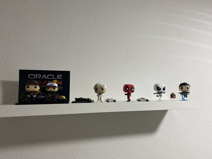 A white shelf displaying an Oracle Red Bull Racing Funko Pop display, Deadpool, Storm, and Superman figures, along with miniature cars.