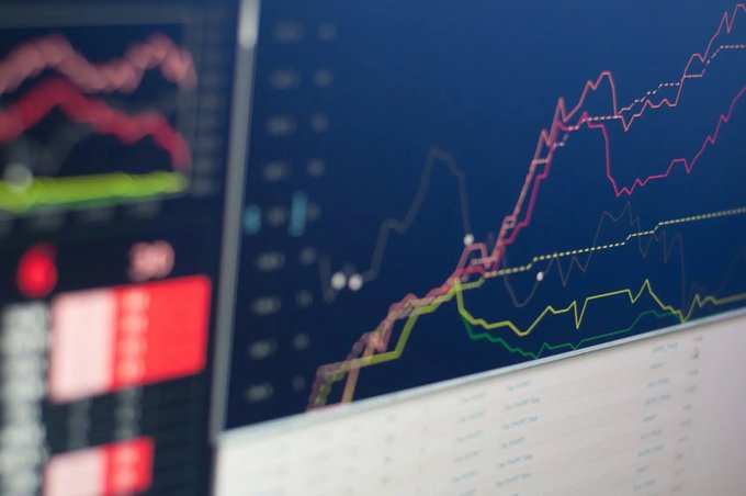 A close-up photograph of trading charts with pink, red, and green lines on a dark blue background, accompanied by a partial data panel on the left showing red and green indicators. The image visually reinforces the post's topic of corporate Bitcoin treasuries by depicting financial market tracking, though no specific text, numbers, or tickers are legible in the charts.