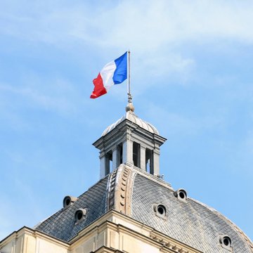 The image shows a building with a flag flying atop its roof. The flag has red, white, and blue colors, which are the colors of the French national flag. The building appears to be an old structure, possibly a church or a historical site in Paris. In the background, there is some text that reads "LATEST: Paris-listed Bitcoin treasury firm Capital B is developing a BTC-backed credit product for Europe, targeting double-digit yields." This suggests that the image might have been taken during a time when cryptocurrency was gaining popularity and becoming more accessible to the general public. The presence of the flag on top of the building could be an indication of its historical or cultural significance in Paris.