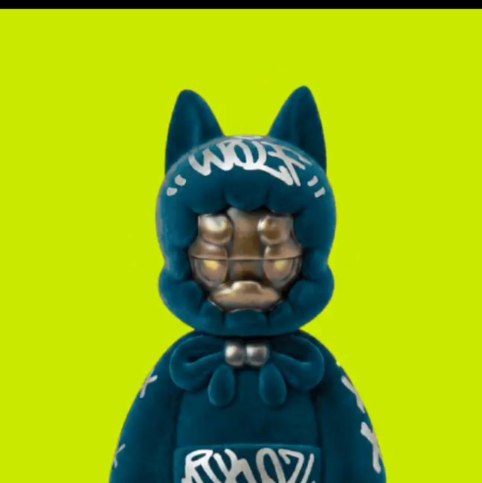 A dark teal stylized figurine with cat ears, glowing eyes, and graffiti-style text including 'WOLFY' on its hood against a bright green background.