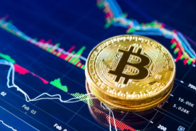 A physical Bitcoin token rests on a financial chart displaying colorful candlestick patterns and a downward-trending line graph, visually reinforcing the story of a long-dormant early Bitcoin wallet awakening to move 100 BTC—now worth roughly $8.55 million—that were acquired when BTC's value was once negligible.