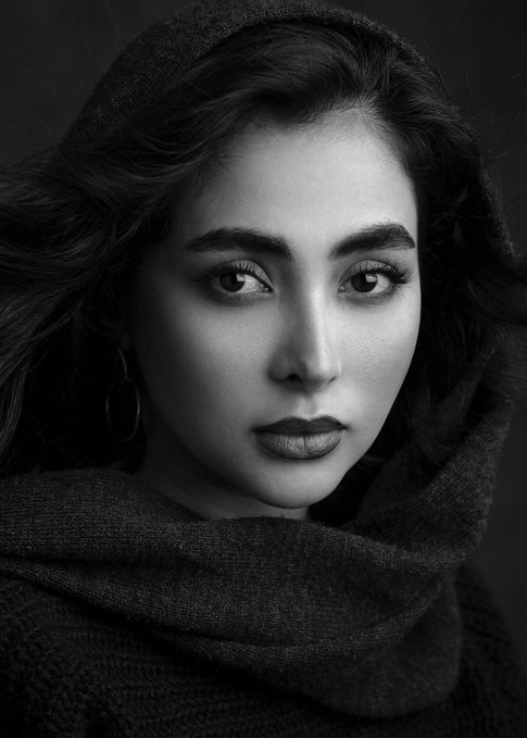 A black-and-white portrait of a woman with striking features, wearing a hooded dark textured shawl, gazes directly at the viewer. The image evokes the mystical, artistic aesthetic fitting for a "Mehrak" 1/1 edition NFT celebrating #TezosTuesday.