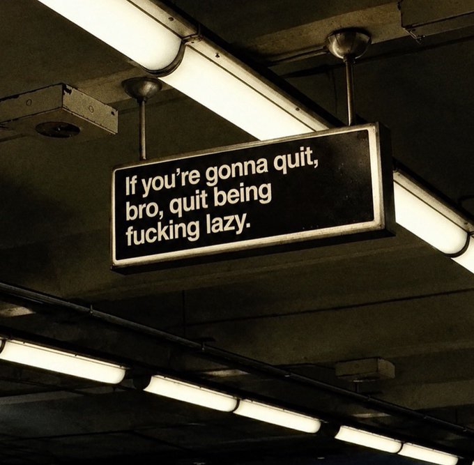 A sign hanging from an industrial ceiling reads "If you're gonna quit, bro, quit being fucking lazy." The blunt motivational message ties into the post's theme of persistence, urging the viewer not to give up out of laziness but to keep pushing through.