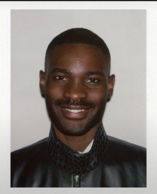 Vintage-style portrait photograph of a smiling Black man wearing a dark jacket with a patterned scarf, resembling a graduation photo.
