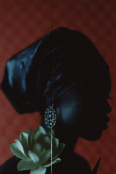 The image features a woman with her head turned to the side, wearing a black headscarf or turban. She has a white flower attached to her hair, adding an interesting visual element to the scene. The background of the photo appears to be red, which contrasts with the white flower and the black headscarf. There is also text in the image that reads "Mirage A new 1/1 @TransientLabs 0.33 ETH". This suggests that the woman might have posted a picture on social media or shared it with friends, possibly related to Mirage brand products.