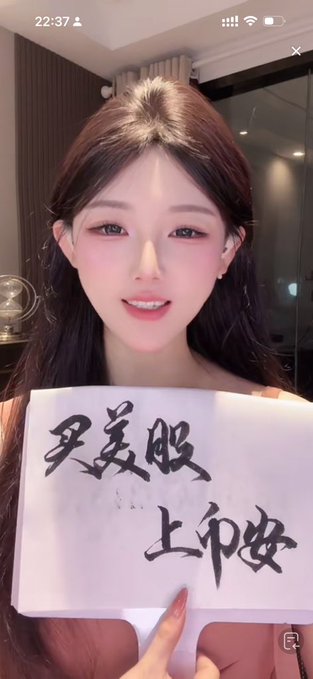 A woman holds up handwritten Chinese calligraphy that reads "买美股 上市啦" (Buy US stocks, listed/go public), jokingly showing off her cousin's handwriting in a playful response to how people address her on Binance.