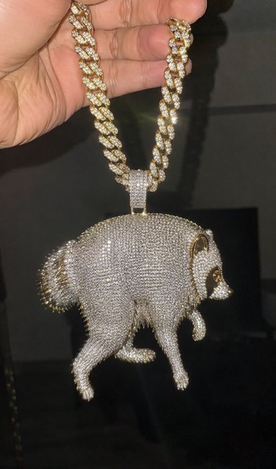 A hand holds up a large, diamond-encrusted pendant shaped like a bulldog hanging from a thick gold Cuban link chain.