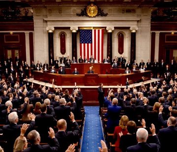 The image shows members of the U.S. House of Representatives gathered in the chamber during what appears to be a formal session or vote, with a large American flag displayed prominently behind the speaker's rostrum. The scene visually underscores the post's message about the CFTC Chair's urgent call for Congress to pass the Clarity Act and establish a federal standard for crypto assets.