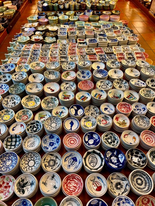 Overhead view of numerous colorful ceramic plates and bowls displayed in rows, featuring various traditional designs including floral patterns and animal motifs.
