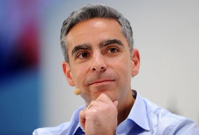 The image features an older man with gray hair wearing a blue shirt, sitting at a desk or table while looking off into the distance. The man's hand is placed on his chin as he ponders something. The background of the image includes a blurred wall, suggesting that it could be a room in a building where the photo was taken. The caption provided seems to be unrelated to the main subject and does not provide any additional information about the content or context of the image.