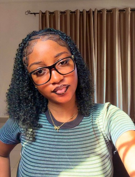 A young woman with curly hair, glasses, and a striped blue top takes a selfie in front of brown curtains, likely identifying herself as "ririonchain," the X user who accused a web3 figure of sharing her photos online without consent and urged others to report the offending account.