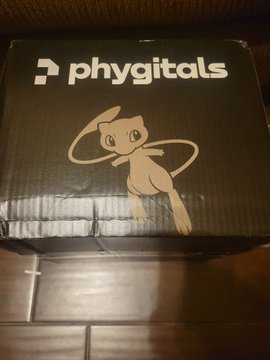 A black shipping box branded with the "phygitals" logo features an illustration of a cartoon rabbit/hare character with a hula hoop. The image relates to the caption "phygi coded" by showcasing the branded packaging of phygitals, a collectibles company.