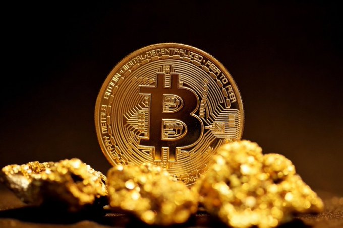 The image features a golden coin sitting next to two rocks that are also golden. The coins appear to be made of metal or have some sort of metallic sheen. The background is black, which contrasts with the golden objects. The text "FED CHAIR KEVIN WARSH about Bitcoin" suggests that there might be a connection between the golden coin and Bitcoin, possibly as a symbol of their value or significance in the world of cryptocurrency.