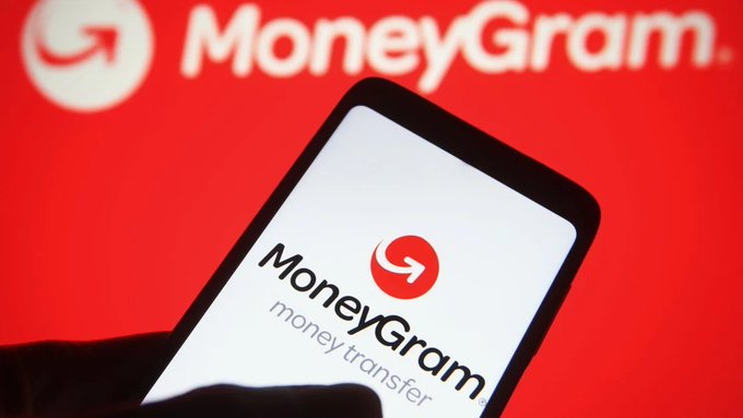 The image shows a person holding up their phone displaying the MoneyGram app. The app features a new stablecoin called MGUSD, which allows users to hold and transfer digital dollars through the MoneyGram app. This new feature will be available in the United States first before expanding across other countries.