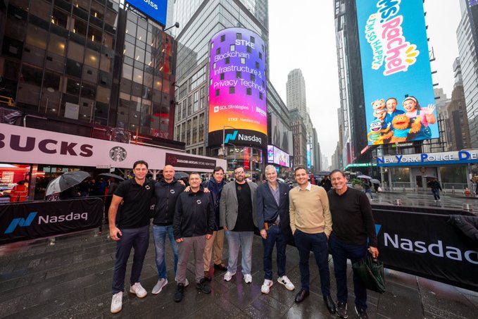 The management team of SOL Strategies poses together in Times Square at the Nasdaq Exchange, with the iconic Nasdaq tower displaying the "$STKE Blockchain Infrastructure & Privacy Technology" branding to celebrate their milestone. The image captures their achievement of being featured on the Nasdaq display in New York City, marking a proud moment for the company.