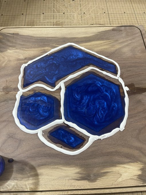 A wooden cutting board displaying blue and white resin art pieces with white borders, resembling polished gemstones in various geometric shapes.