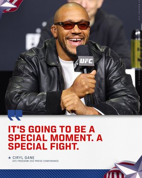 The image features a man wearing sunglasses, sitting at a table with a microphone in front of him. The background includes an American flag and a banner that reads " UFC Freedom 250 | Live on @ParamountPlus | Presented by @cryptocom & @RamTrucks". The man is smiling and appears to be talking into the microphone during a press conference or event, possibly discussing the upcoming UFC fight.