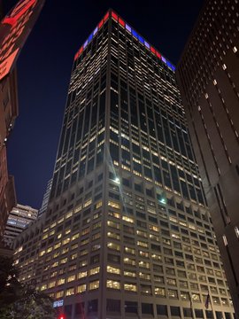 A nighttime upward view of a brightly lit skyscraper with red "Bank of America" signage at the top, fitting the "$LINK IYKYK" post referencing Bank of America.