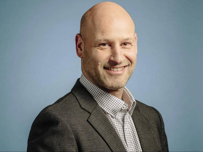 A bald, smiling man in a gray blazer and checkered shirt poses for a professional headshot against a gray backdrop. The accompanying post about SharpLink's $SBET Ethereum staking milestone likely features him as a company executive or representative.