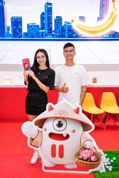 A woman and a man wearing white "TRON" t-shirts pose with a red phone and a thumbs-up beside a large TRON mascot at the Conviction 2026 event, with the TRON logo visible on the booth backdrop, reflecting the post's praise for the team's polished branding and community experience.