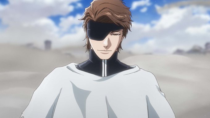 An anime character with brown hair and an eyepatch winks at the camera while wearing a white hooded robe against a desert backdrop.