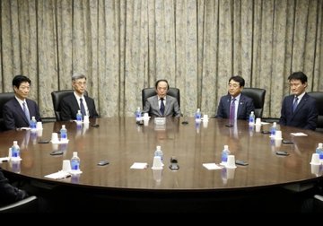 Five men in dark suits seated around a long wooden conference table, appearing to be in a formal meeting or political discussion.