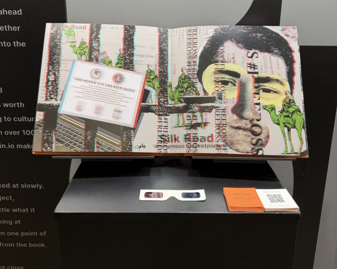 A display case featuring an artwork titled 'Milk Road' with the headline 'THIS HIDDEN SITE HAS BEEN SEIZED' overlaid on what appears to be a manipulated Silk Road page, alongside 3D glasses and an orange 'Project History' booklet.