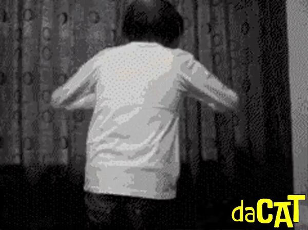 The image features a person wearing a white shirt, standing against a curtain with their back facing the camera. The caption of the photo reads "Good Wednesday and happy hump day $daCAT fam! Time to wake up and get after it!". This suggests that the person is dressed for a casual or relaxed day, possibly enjoying some downtime at home.