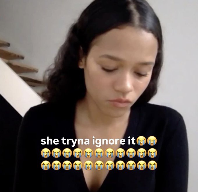 A woman with dark hair and a black top looks down with a serious expression, overlaid with the text 'she tryna ignore it' followed by multiple crying face emojis.