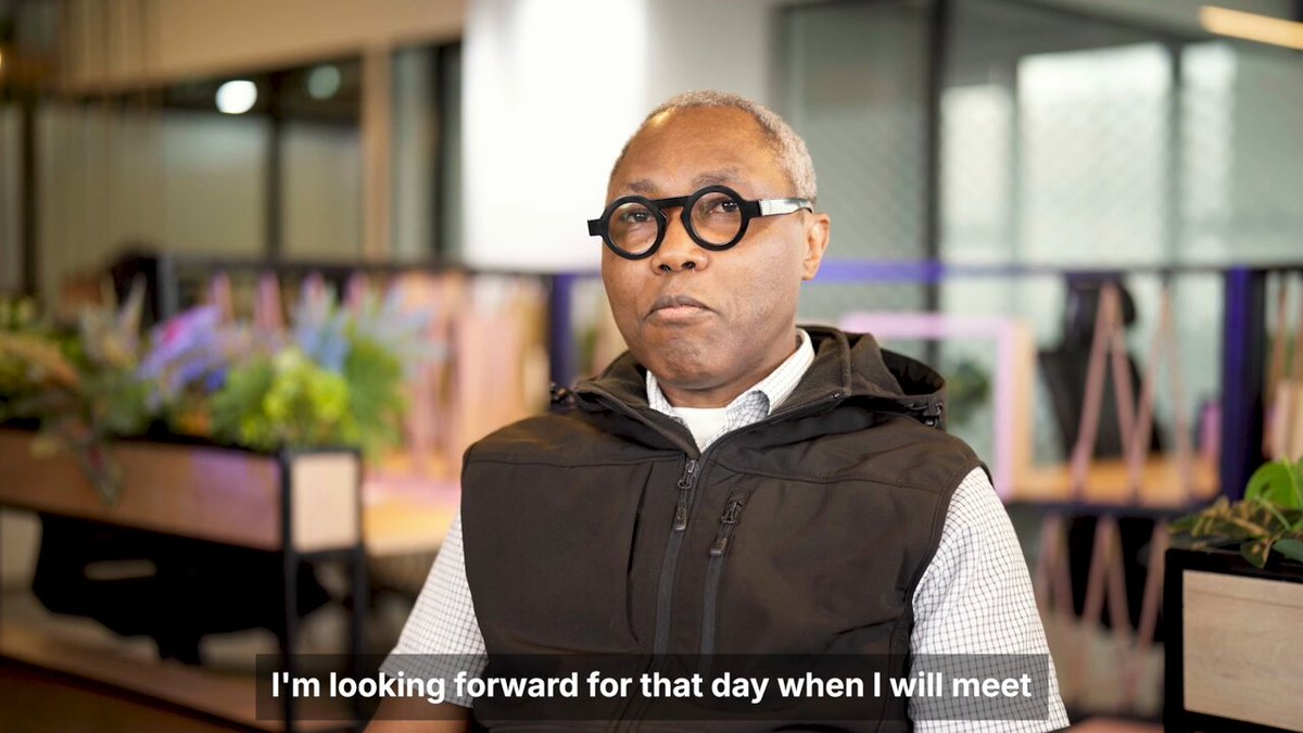 A man wearing round black glasses and a dark vest over a checkered shirt speaks in a modern office setting. The subtitle reads "I'm looking forward for that day when I will meet," accompanying his quote about African markets and regulatory simplification through ADAPT.