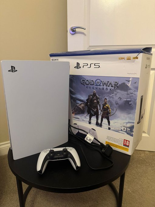 A PlayStation 5 console with controller and God of War Ragnarok box displayed on a small black table.