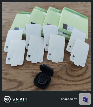 Multiple white blank cards or tags fanned out on a wooden surface with green packaging boxes and a small black circular device, watermarked 'SNPIT'.