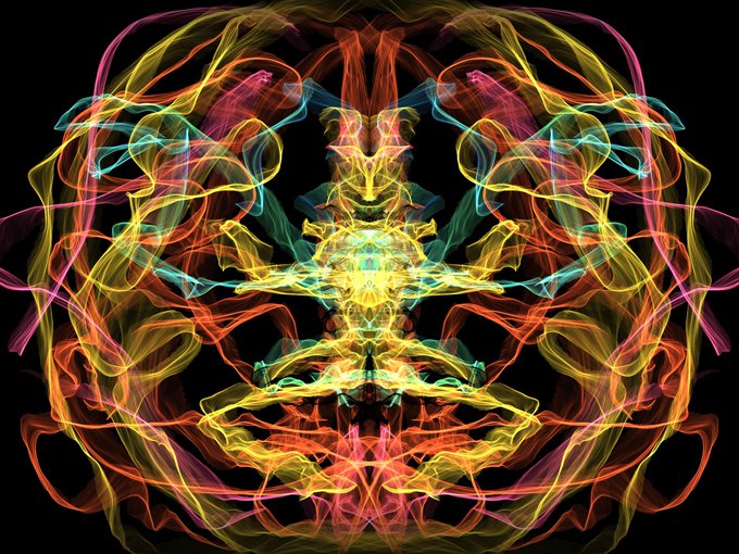 A symmetrical abstract digital artwork featuring swirling, wispy trails of red, yellow, pink, and cyan light forming an intricate, mask-like pattern against a black background.
