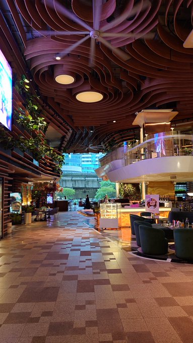 An interior view of a modern, stylish restaurant or lounge with a striking sculptural wooden ceiling, patterned tile flooring, and ambient lighting.