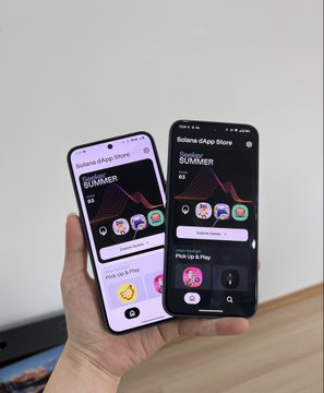A hand holds up two Solana Seeker smartphones side by side, both displaying the Solana dApp Store homepage featuring the "SUMMER" event countdown and "Pick Up & Play" options, celebrating the arrival of a second Seeker device from Solana Mobile.