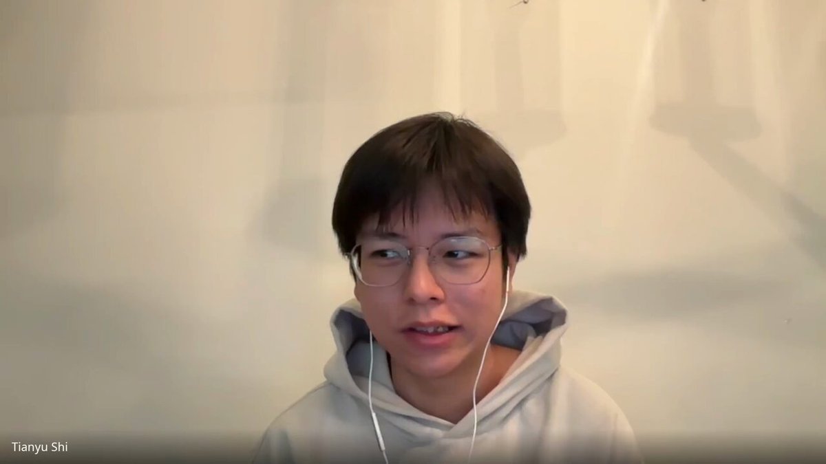 The image shows a person wearing glasses, possibly a young man with short hair, who appears to be talking into a microphone or headset. The background of the image is white, which contrasts with the person's dark hair. There are no other objects in the image besides the person and their audio equipment.