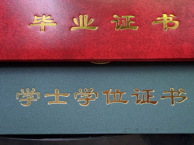 Two Chinese academic certificate covers are stacked, with the red one on top embossed in gold with "毕业证书" (Graduation Certificate) and the dark green one below reading "学士学位证书" (Bachelor's Degree Certificate), symbolizing the user's recent academic milestone.