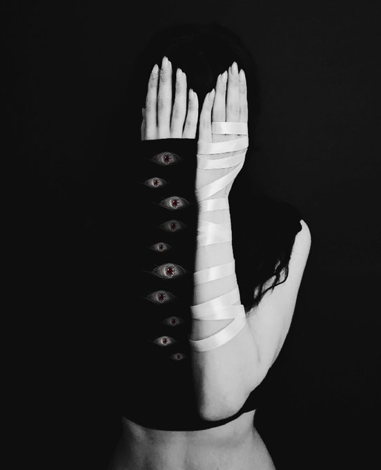 A black and white surrealist image showing a person with hands covering their face, featuring an eye-pattern design on the arm and bandages wrapped around the hand.