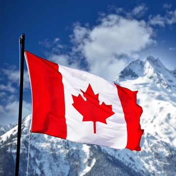 The Canadian flag waving against a backdrop of snow-capped mountains and a blue sky.