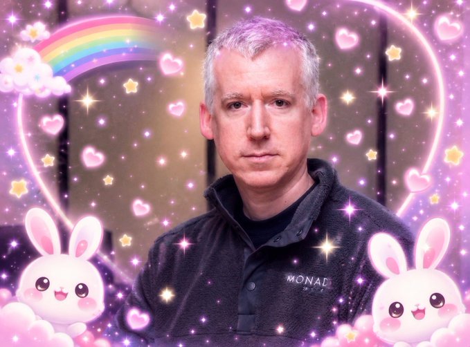 A man wearing a 'MONAD' branded jacket is surrounded by a decorative pink border featuring cartoon bunnies, hearts, stars, and a rainbow.