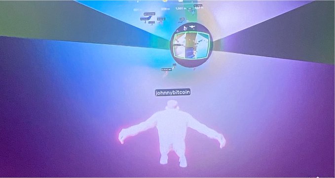 A glowing white humanoid character labeled "johnnybitcoin" floats in a vibrant blue and purple virtual environment, with a circular portal display and game interface visible above. The image appears to be a screenshot from the game by @OtherGamesXYZ, showcasing a gameplay moment featuring the named avatar in a colorful, immersive setting.