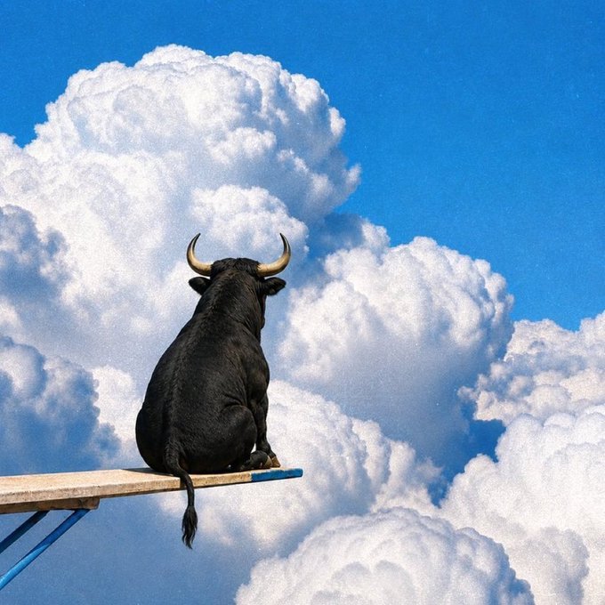 A surreal photograph of a black bull with horns sitting on a wooden diving board, gazing up at a bright blue sky filled with large, fluffy white clouds.